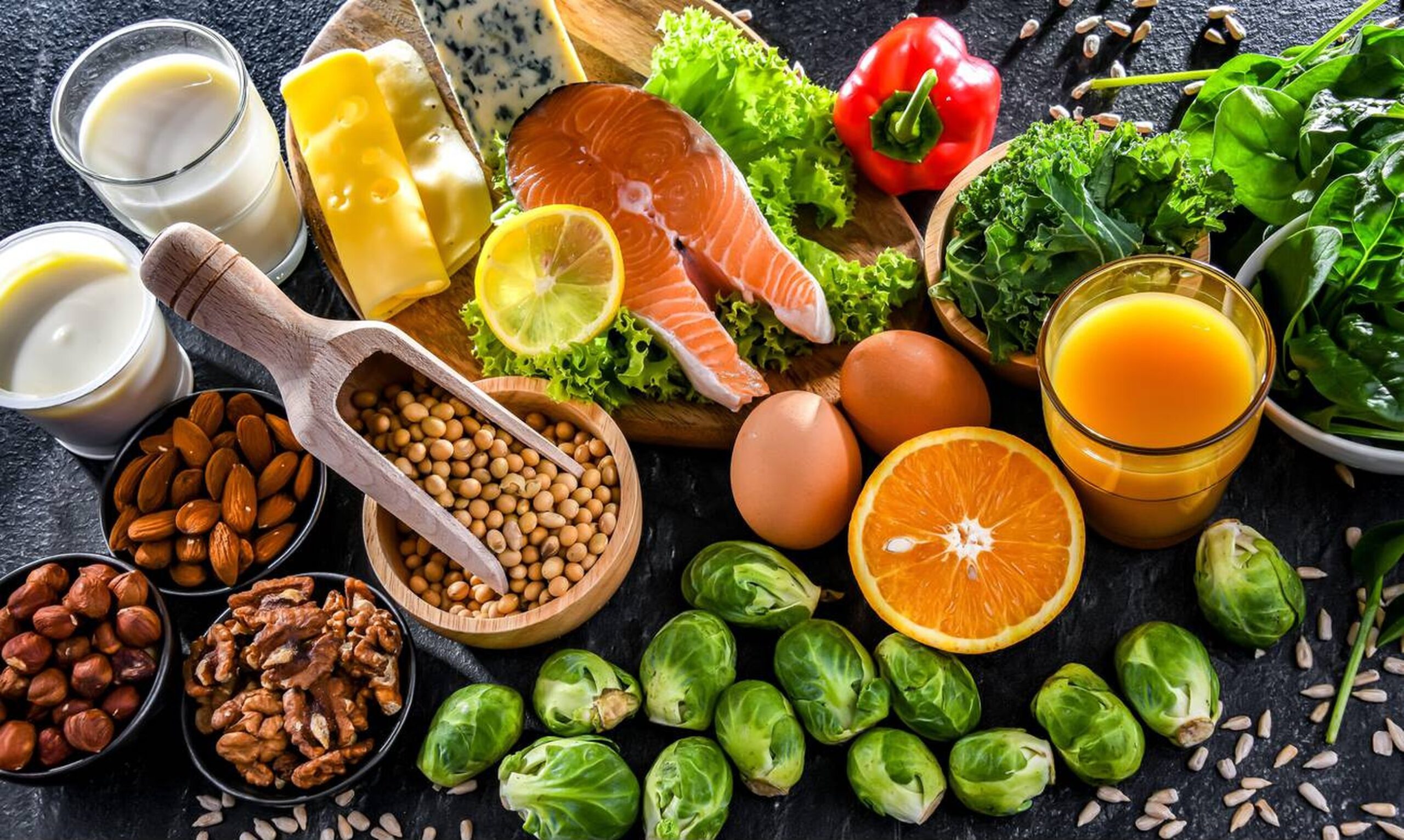 A colorful arrangement of bone-strengthening foods including salmon, kale, almonds, milk, and yogurt on a wooden table.